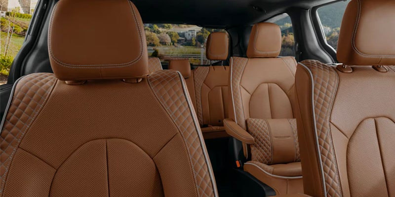 Interior view of a car with two rows of tan leather seats, with quilted accents and white piping.