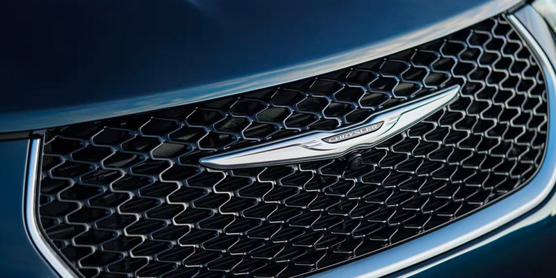 Close-up of a dark blue car's grille, featuring a silver Chrysler logo in the center and a small camera below it.