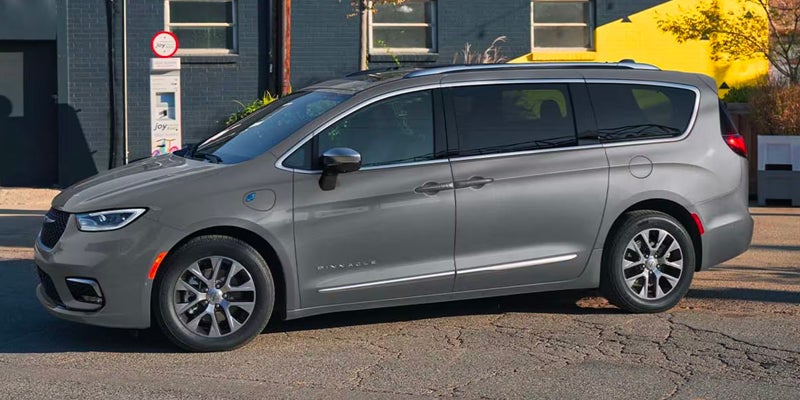 Side view of a gray Chrysler Pacifica Hybrid minivan parked on a street next to a building.
