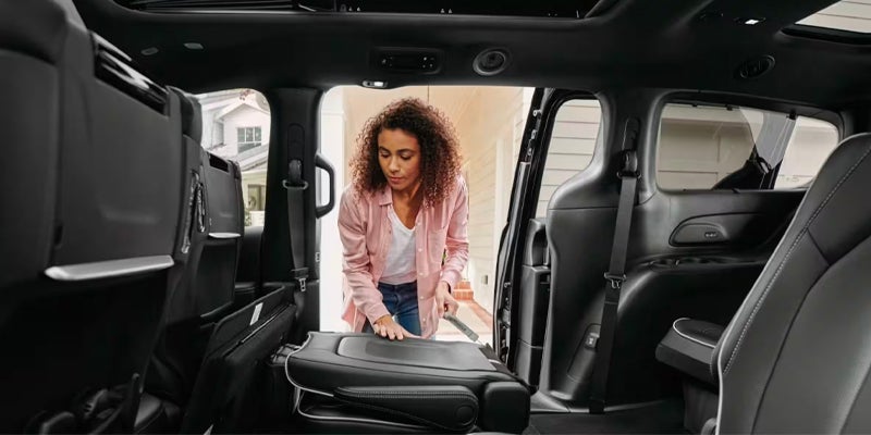 Woman with curly hair folding a minivan seat to store it in the floor compartment.