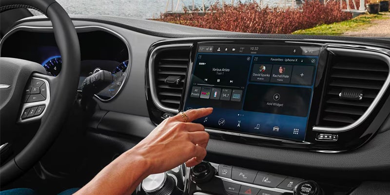 A person's hand with rings tapping the touchscreen dashboard of a car.