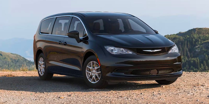 Black Chrysler Pacifica minivan parked on a dirt road with mountains in the background.