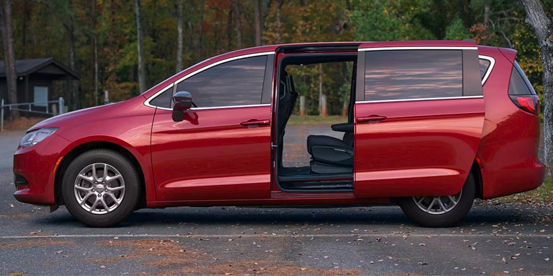 Red van with the passenger side sliding door open, revealing black seats inside, parked on asphalt.