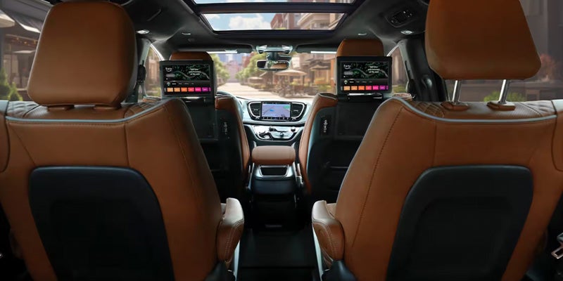 Interior of a car's second-row seats, tan leather with media screens on the back of the front seats.