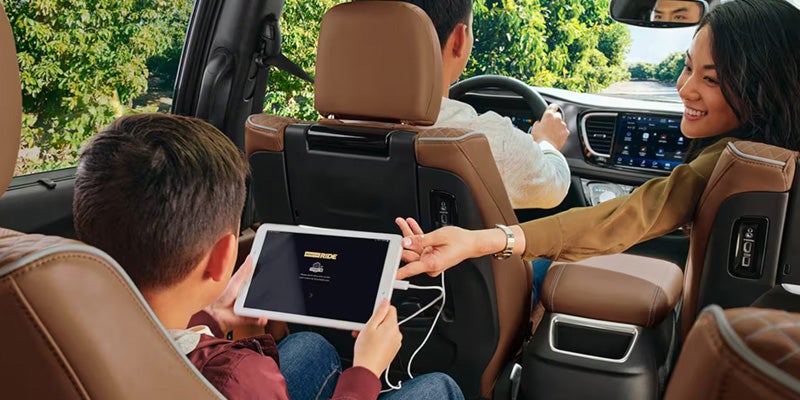 Family in a car. A mother helps her child with a tablet, sitting behind the dad who is driving.