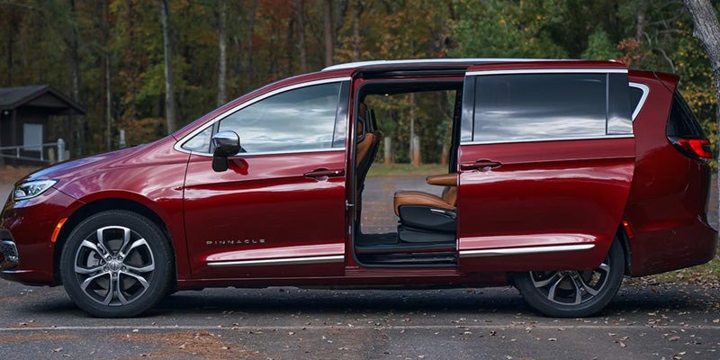 Side view of a red minivan with its passenger side sliding door open, revealing a tan interior.