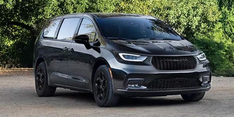 Black Chrysler Pacifica minivan parked on a dirt road with green foliage in the background.