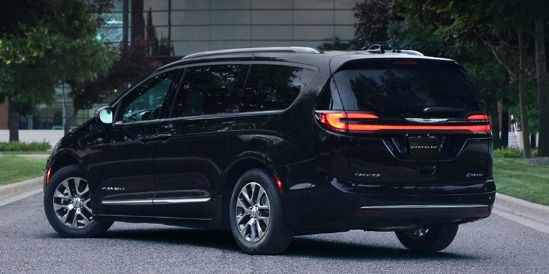 A black Chrysler Pacifica minivan, seen from the rear passenger side, parked on a paved road.
