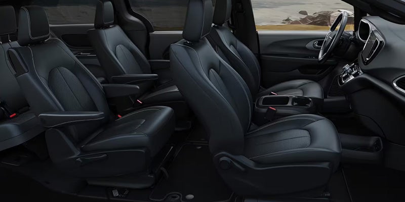 Interior view of a vehicle showing multiple rows of dark leather seats with light stitching and the driver's area.
