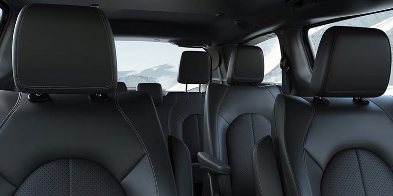 Interior view of a car, showing multiple rows of black leather seats with white stitching and textured inserts.