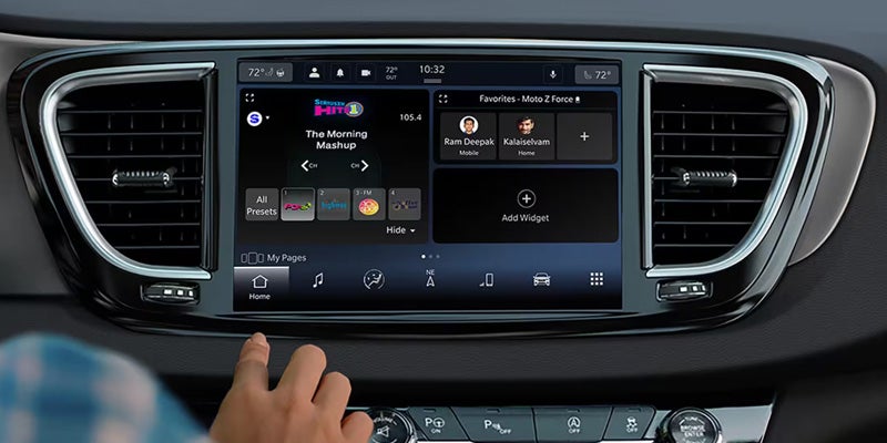 A hand interacts with a car's infotainment touchscreen, displaying radio "The Morning Mashup" and "Favorites" for phone contacts.