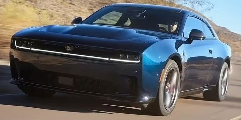 Front-left of a dark blue Dodge Charger cruising down a desert highway under a clear sky.