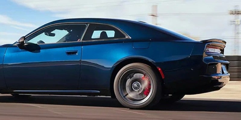 Dark blue two-door sports car in motion, viewed from the rear passenger side, with blurred background.