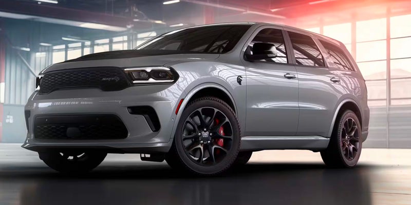 A light gray Dodge Durango SRT Hellcat SUV with a black hood and wheels, in a garage.