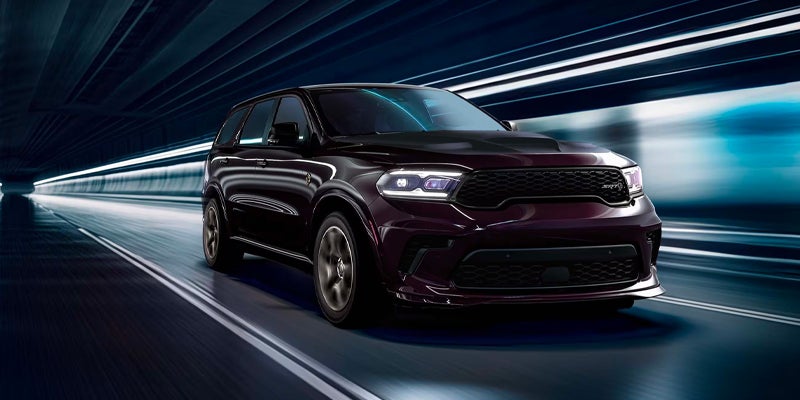 Maroon SUV with bright headlights speeding down a dark, futuristic tunnel with blurred lights on the walls.
