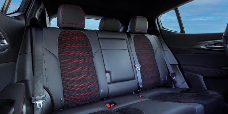 Back seats of a car with black leather and red striped fabric in the center cushions and red stitching.