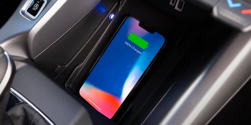 A smartphone with "100% Charged" on its screen lies on a car's wireless charging pad.