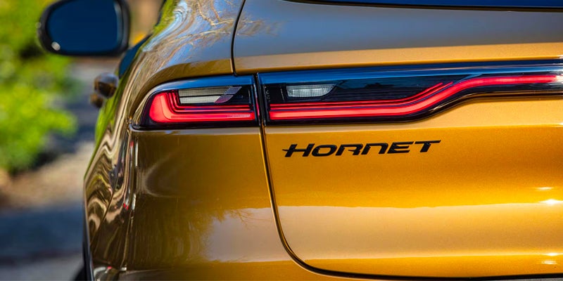 A close-up of the rear of a golden-yellow Dodge Hornet, showing illuminated red taillights and the black HORNET badge.