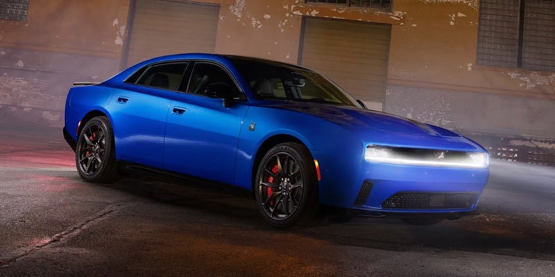 Bright blue Dodge Charger sits parked on asphalt at night with a tan building in the background.