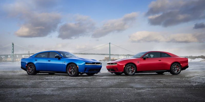 Blue four-door and red two-door coupes with a bridge in the background, parked on a wet, gray surface.