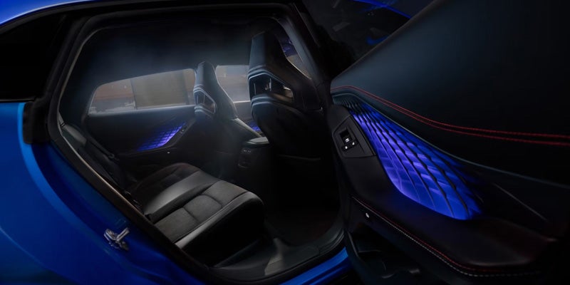 Car interior with open door, showing black seats, blue ambient lighting on door panels and dashboard.