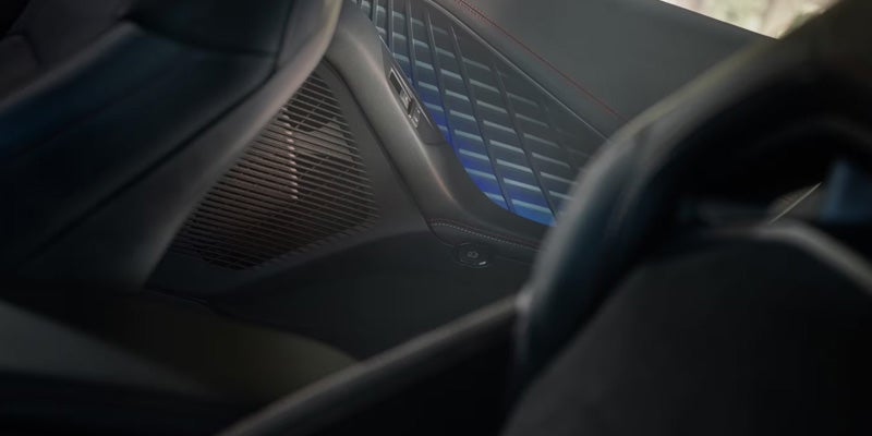 Car interior showing a dark seat, speaker grille, and decorative door panel with blue ambient lighting.