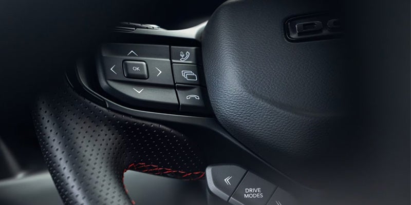 Close-up of a car's black leather steering wheel with red stitching details and control buttons.