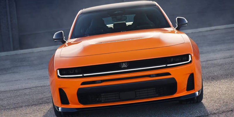 Front view of an orange Dodge Charger Daytona SRT EV concept car on asphalt, with black roof and grille.