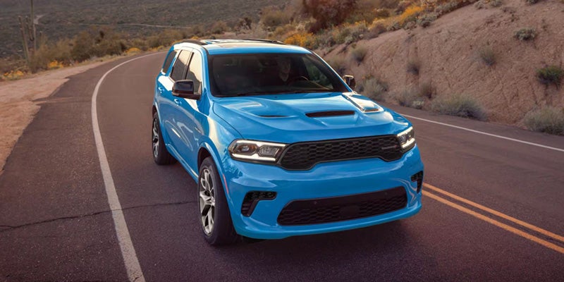 A bright blue SUV driving on a winding desert road with mountains and brush in the background.
