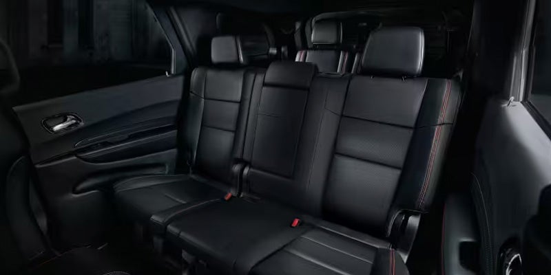 Three rows of dark leather car seats with red stitching and black door panels with silver handles.
