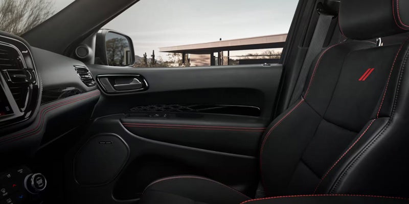 Interior of a dark car with black leather seats and red stitching, door, and dashboard with a building outside.