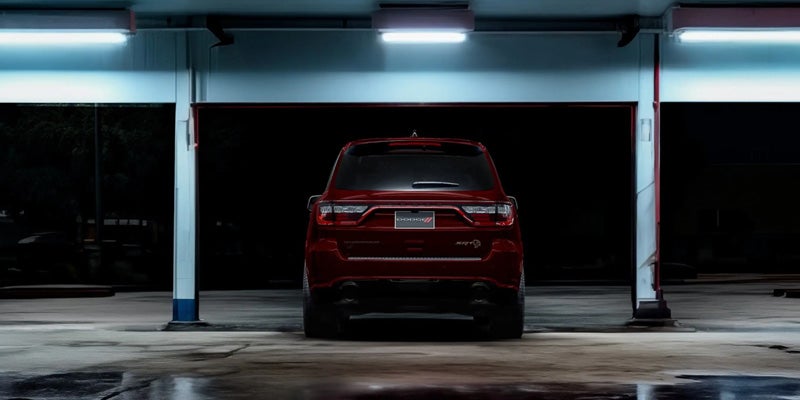 Rear view of a red Dodge Durango SRT parked inside a garage at night, illuminated by fluorescent lights.