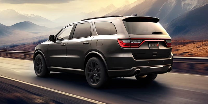 Dark gray Dodge Durango SUV driving away on a highway with hazy mountains in the background under a sunset sky.