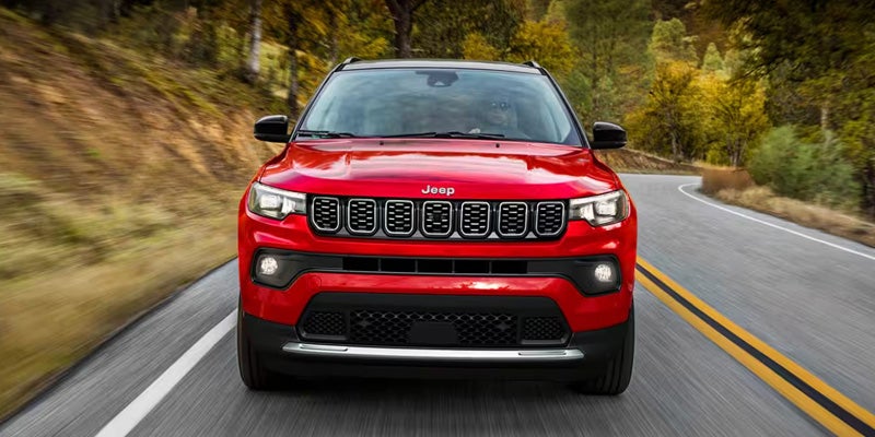 A red Jeep Compass drives down a winding road with trees in the background.