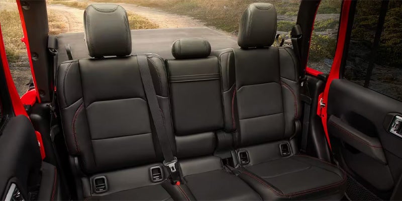 View from the back of a red car, showing three black leather rear seats with red stitching