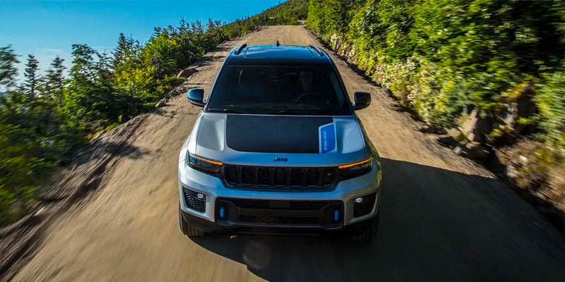 Front view of a silver Grand Cherokee 4xe with a matte black hood stripe driving up a winding dirt road.