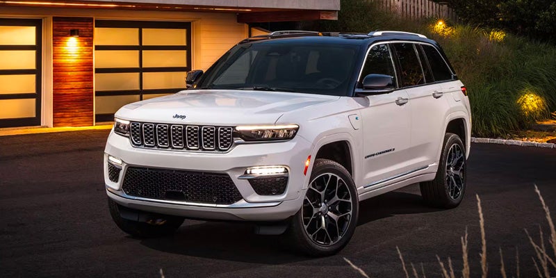 A white Jeep Grand Cherokee, with a black roof, parked on a driveway in front of a modern garage at dusk.