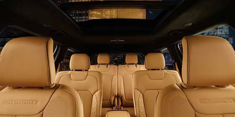 Vehicle interior featuring tan leather seats in three rows, with "SUMMIT" embroidered on the front seat.