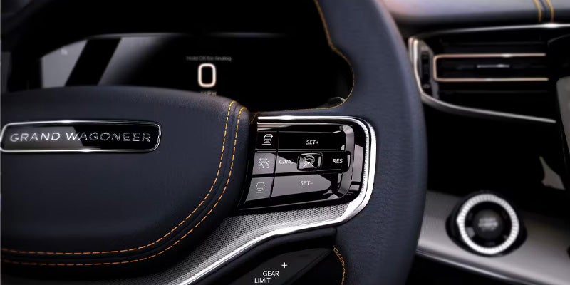 Close-up of a Grand Wagoneer steering wheel with "GRAND WAGONEER" embossed, control buttons, and orange stitching.