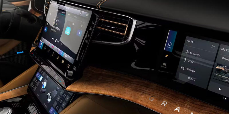 Interior close-up of a luxury car dashboard showing two large touchscreen displays and a wood-grain accent.