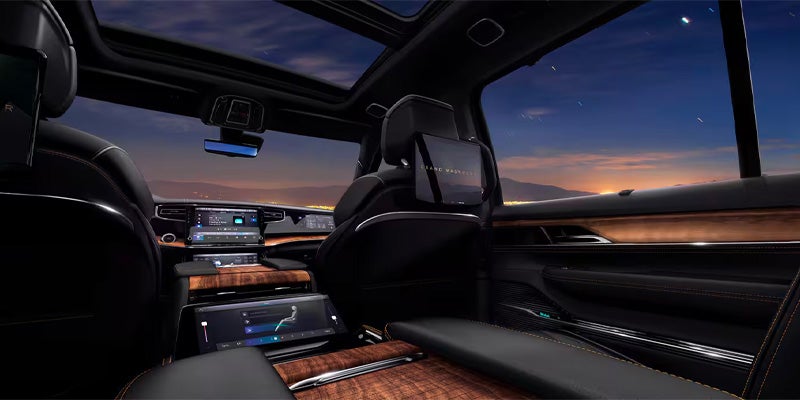 The luxurious interior of a car at dusk, with digital screens, wood trim, and a mountain landscape visible through the windows.