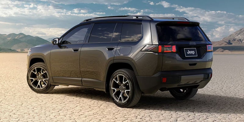 Rear view of a dark gray Jeep Grand Cherokee Laredo parked in a vast, dry desert landscape with mountains.