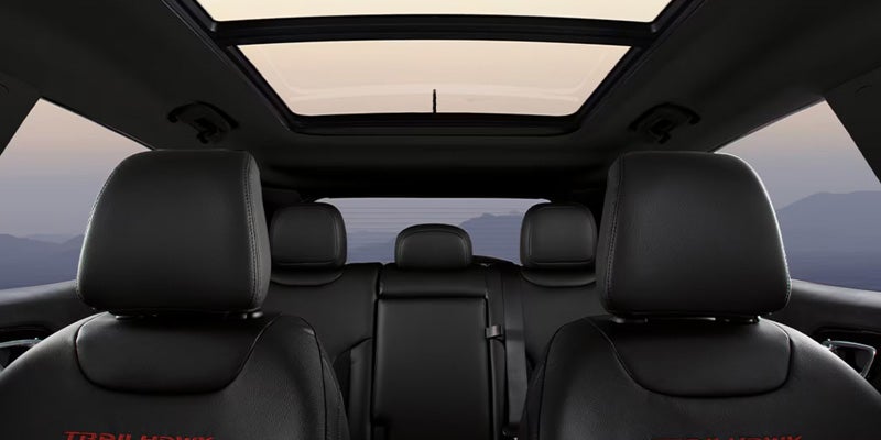 Car's interior with black leather seats, a large sunroof, and a mountainous landscape visible through the windows.