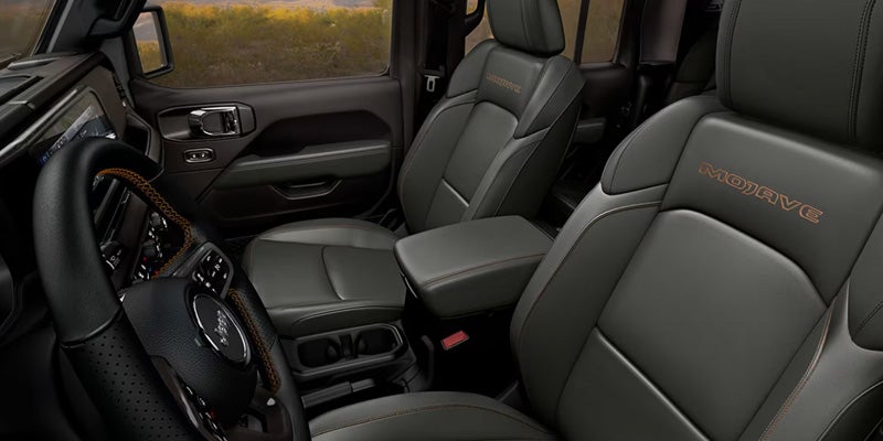 Interior of a dark grey Jeep Gladiator with "MOJAVE" embroidered on the seats and an orange-stitched steering wheel.