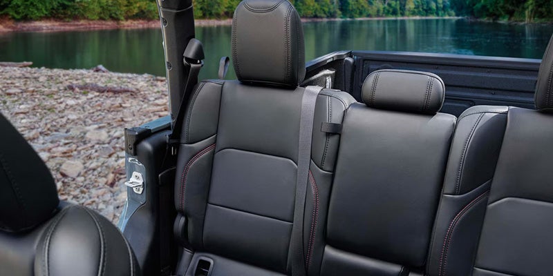 Interior view of a vehicle, showing black leather seats with red stitching, overlooking a lake and trees.