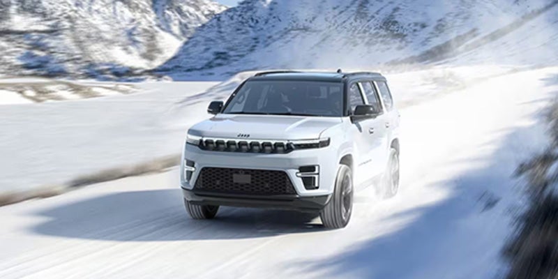 White Jeep Wagoneer SUV on a snowy mountain road, motion blur implying speed and winter conditions.