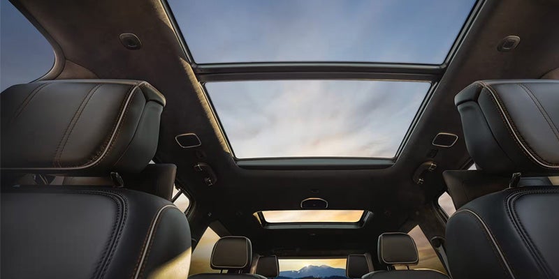 Interior view of a car with a panoramic sunroof, showing two rows of black leather seats and a cloudy sky.