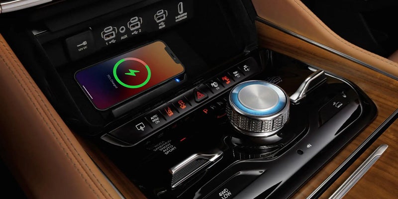 A smartphone wirelessly charging in a luxurious car interior with a chrome gear selector and wood trim.