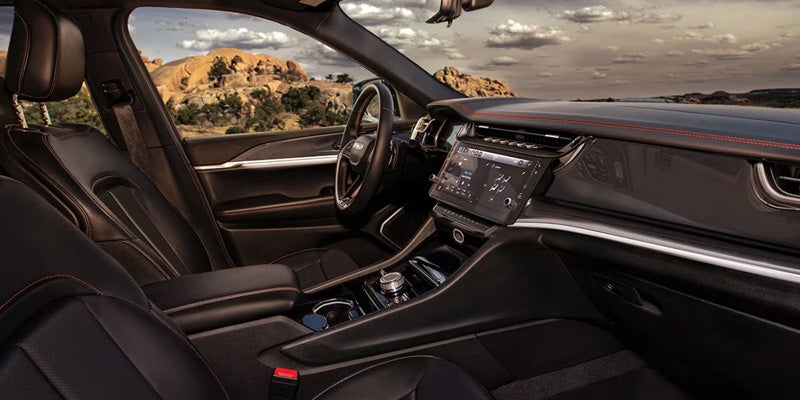 Interior view of a car with black leather seats and red stitching, a large touchscreen, and a rocky desert visible outside.