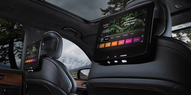 Two rear-facing infotainment screens with "Fire TV" displayed are mounted on the back of car seats.